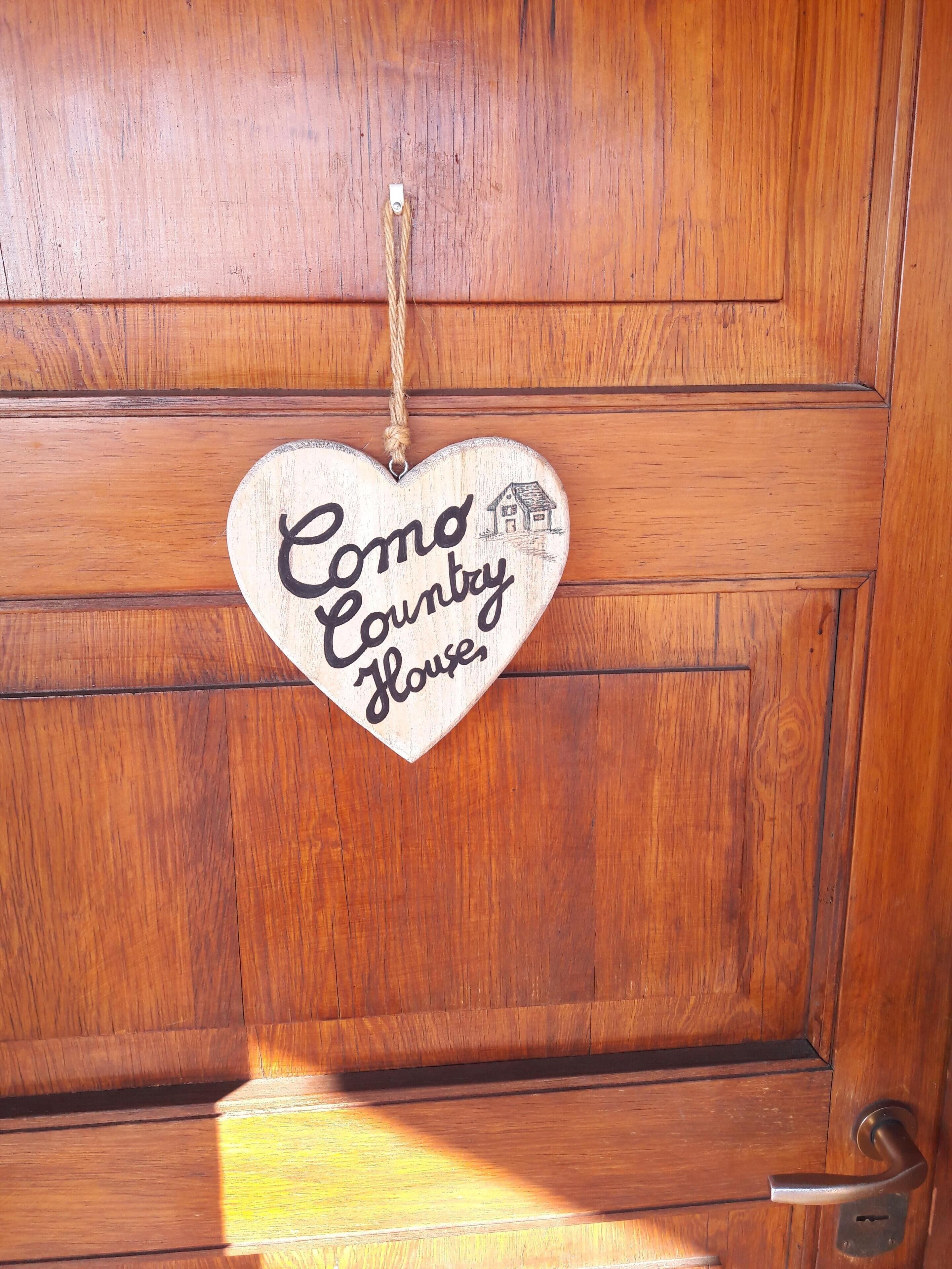 Une porte en bois ornée d’une plaque en forme de cœur sur laquelle on peut lire : « Como Country House ».