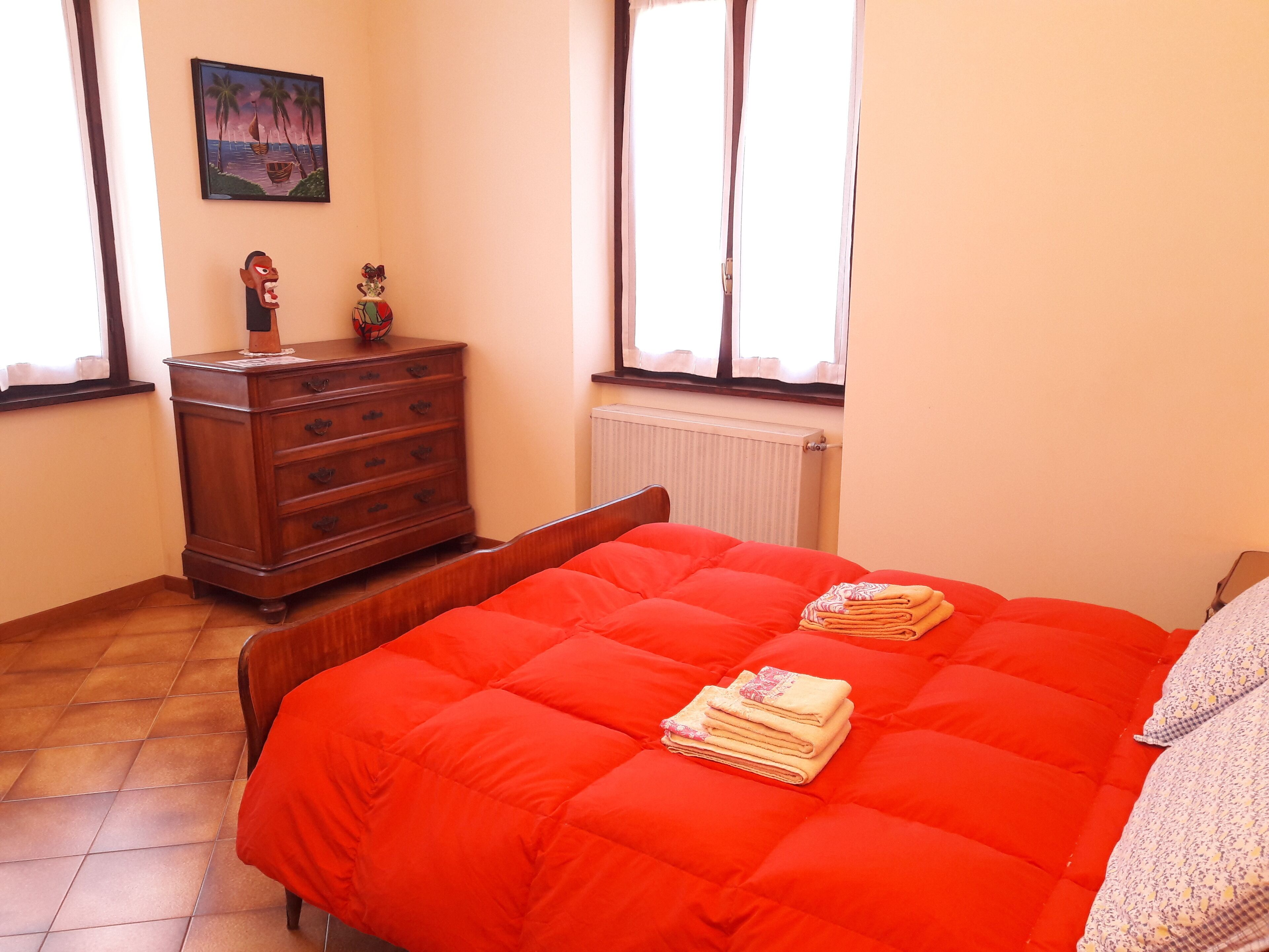 Ein Schlafzimmer mit Bett, Kommode, Heizkörper und einem fensterbepflanzten Fenster.