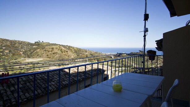 A balcony with a table, a potted plant, and a view of the sea and hills. - Casa Annunziata Badolato, Borgo, Mare and Olive Harvest (Badolato)