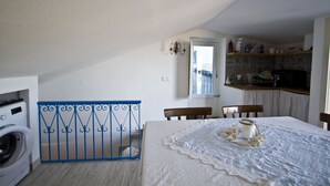 A room with a washing machine, a blue metal gate, a dining table with a white tablecloth, and a kitchen area with a window. - Casa Annunziata Badolato, Borgo, Mare and Olive Harvest (Badolato)