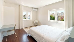 A modern bedroom with a bed, a desk, a chair, and two windows offering city views. - Apartment 4 bedrooms (2) - Porto (Porto)
