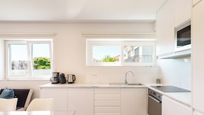 A modern kitchen with white cabinets, a built-in oven, a microwave, and a window overlooking a green area. - Apartment 4 bedrooms (2) - Porto (Porto)