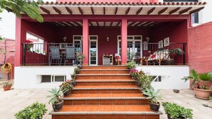 A building with a red exterior, a covered porch with steps, and potted plants. - Casa El Tonelero with garden and private pool (Gáldar)