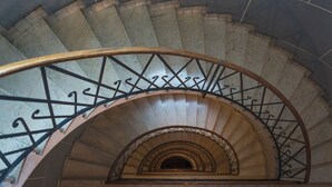 Un escalier en colimaçon avec une rampe en bois et des balustres en métal.