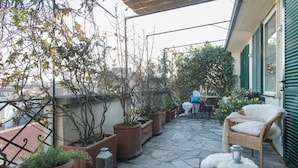 Une terrasse dallée de pierres, agrémentée de plantes en pot, de meubles en osier et d’une table avec des chaises.