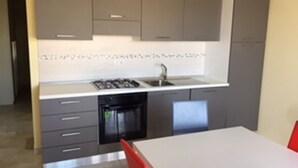 Una cocina moderna con gabinetes grises, encimera blanca, horno empotrado y un lavamanos.