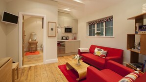 Een moderne woonkamer met een rode bank, een houten salontafel en een keuken op de achtergrond.