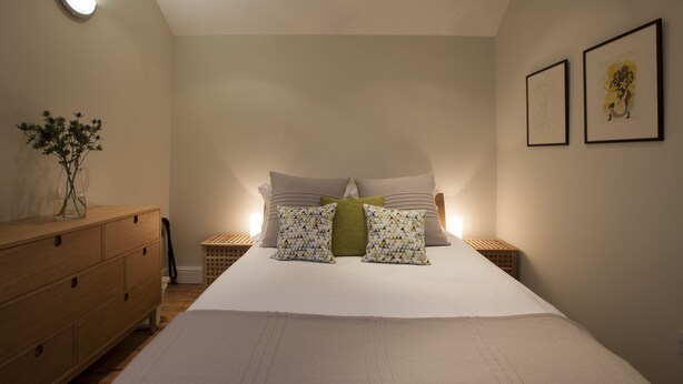 Een slaapkamer met een groot bed, een houten dressoir, nachtkastjes en een kunstwerk aan de muur.