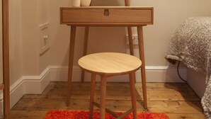 Een houten wastafelmeubel met een ronde spiegel, een klein lade en een kruk.
