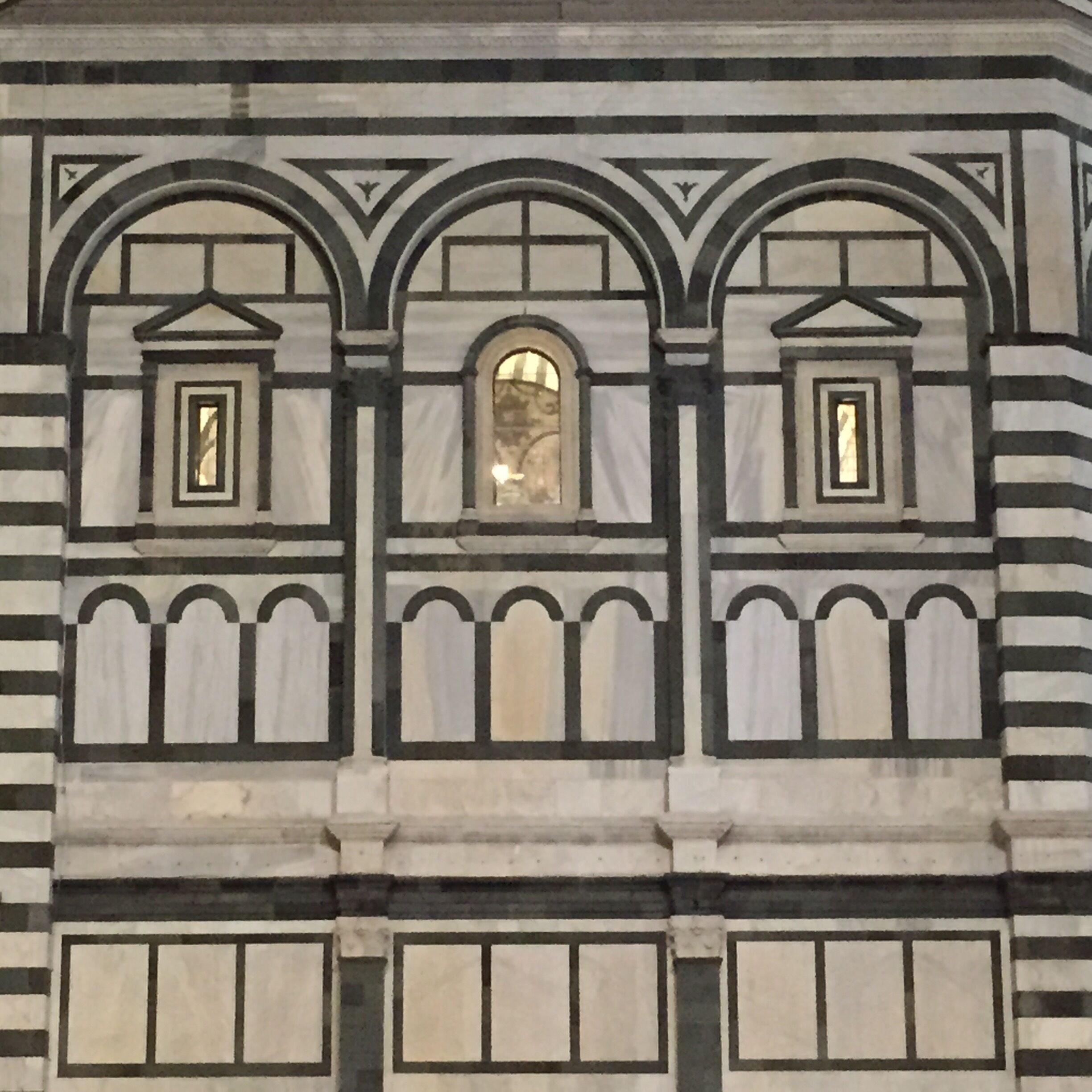 A building facade with three arched windows, each with a small rectangular window above.