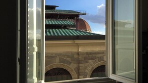 Vista a través de una ventana abierta que muestra un edificio con tejado verde y cúpula de ladrillo.