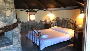 A stone-walled bedroom with a bed, stone fireplace, and two wall-mounted lamps. - Sardinian style holiday home (Quartu Sant'Elena)