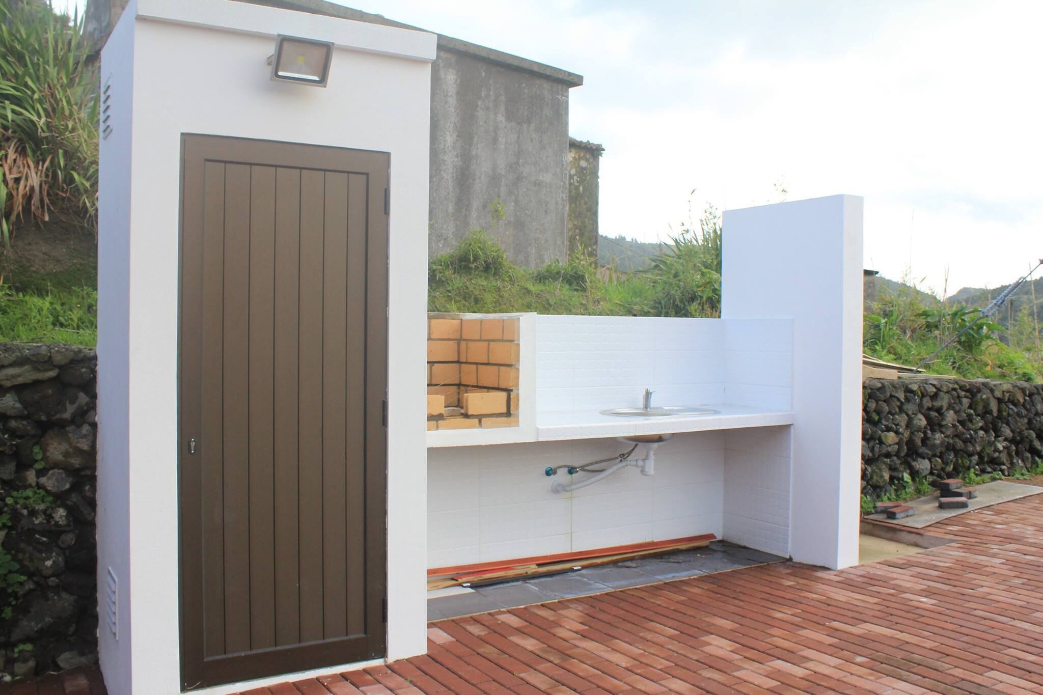 A compact outdoor kitchen area with a built-in sink and a door, surrounded by a stone wall and a wooden deck.