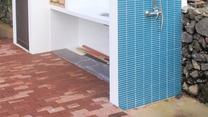 Un espace de douche extérieur moderne, avec un mur recouvert de carreaux bleus, un banc blanc et un mur en pierre.