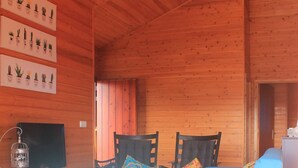 L'intérieur d'un chalet en bois, avec un canapé bleu, deux fauteuils, un téléviseur et une plante décorative fixée au mur.