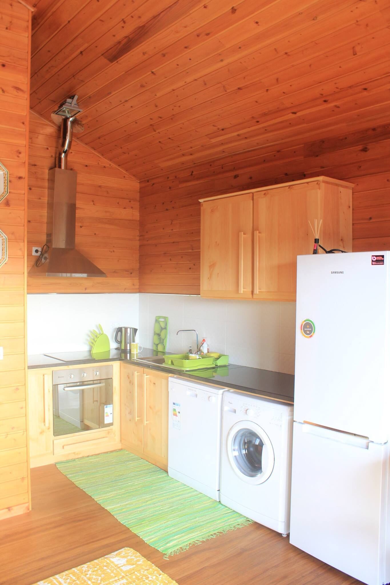 Cocina compacta con armarios de madera, horno de acero inoxidable, lavadora y refrigerador blanco.