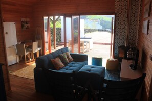 Un acogedor interior de cabaña con un sofá, sillas, una mesita y una zona de cocina.