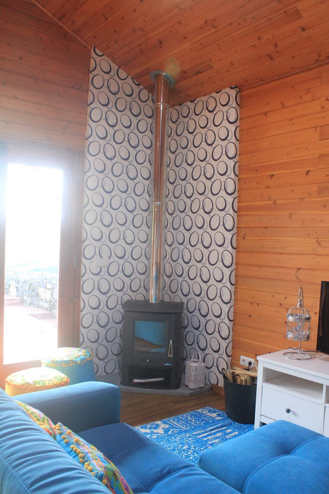 Une pièce chaleureuse avec une cheminée, un canapé bleu, des rideaux à motifs et un plafond en bois.