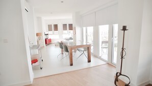 Een ruime zithoek met een houten tafel en stoelen, een rode bank en een vloerlamp.