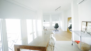 Een lichte, moderne kantoorruimte met een grote glazen tafel, witte stoelen en een metalen kar.