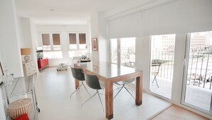 Een ruime woonkamer met een glazen eettafel, moderne stoelen en grote ramen met uitzicht op de stad.