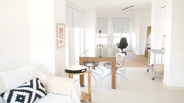 Een lichte, minimalistische woonkamer met een witte bank, een ronde salontafel en een eethoek met een houten tafel en stoelen.
