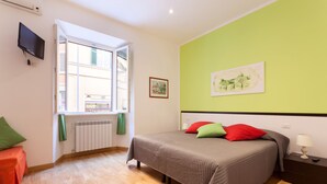 Ein Schlafzimmer mit einem Bett, einem Fenster, einer Heizung, einem Fernseher und einem Bild an der Wand.