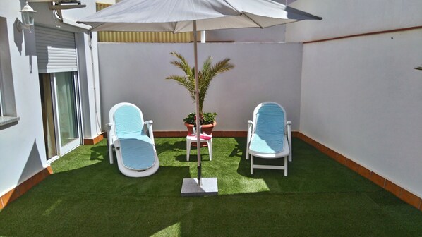 A small patio with two lounge chairs, a table, and a potted plant.