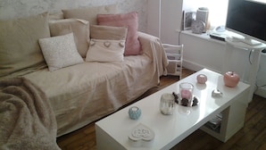 A living room with a beige sofa, a white coffee table, and a television on a stand.
