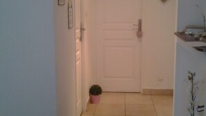 A hallway with a white door, a small potted plant, a heart-shaped decoration, and a shelf with decorative items.