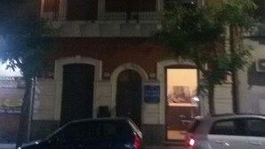 A multi-story building with illuminated windows and doors, a visible entrance, and parked cars in front. - Katane Holidays "Verdi Apartment with Triple Room" (Catania)
