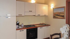 A compact kitchen with white cabinets, a built-in oven, a gas stove, and a sink. There is a wooden ceiling and a framed painting on the wall. - Katane Holidays "Verdi Apartment with Triple Room" (Catania)