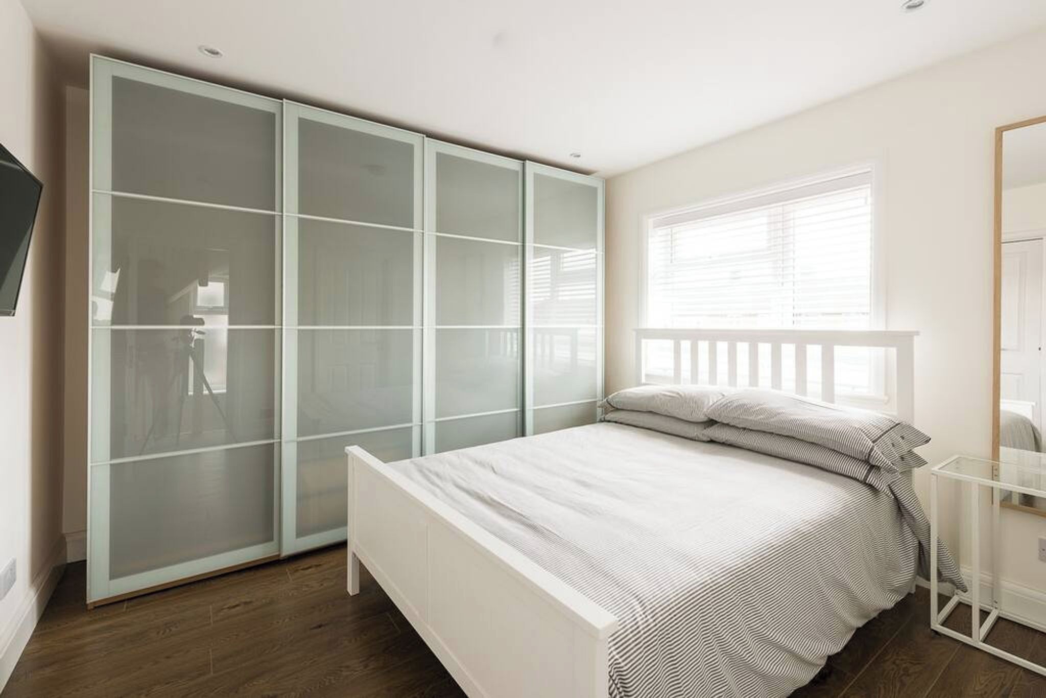 A bedroom with a bed, a wardrobe, a bedside table, and a window with blinds.