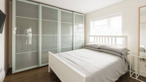 Un dormitorio con cama, armario, mesita de noche y ventana con persianas.