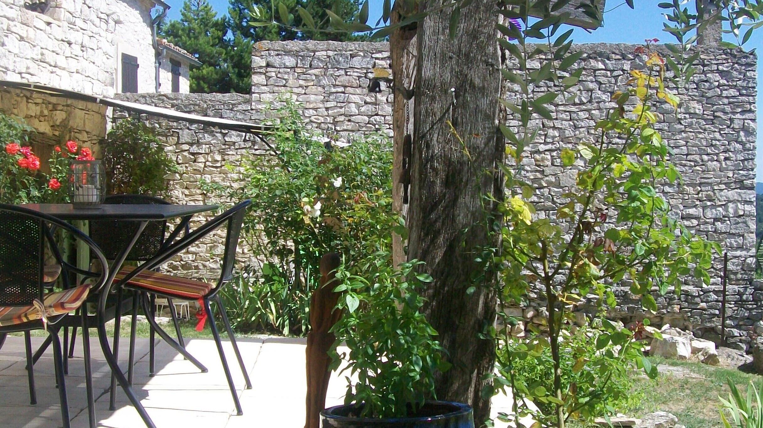 A stone wall, a wooden table with chairs, and a potted plant.