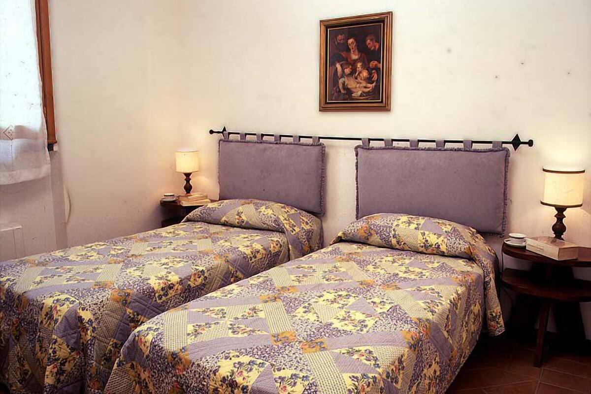 A room with two beds, each with a patterned bedspread and matching pillows. There is a painting on the wall above the beds, and two bedside tables with lamps.