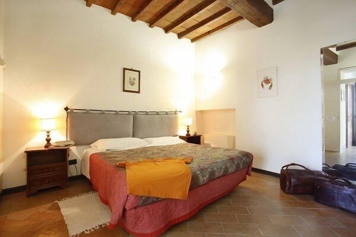A bedroom with a bed, bedside tables, a wooden ceiling, and a door leading to another room.