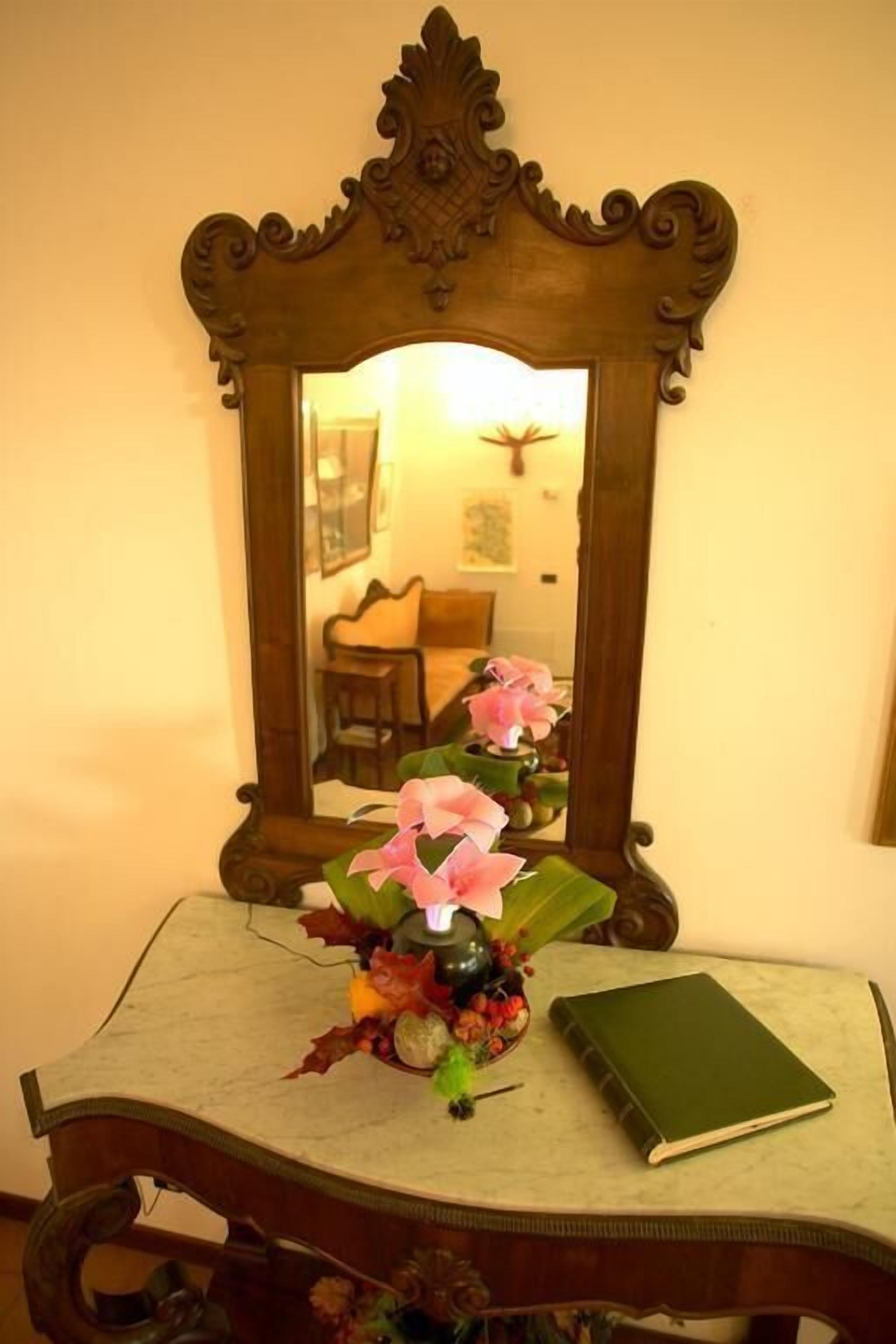 A table with a vase of flowers, a book, and a mirror.
