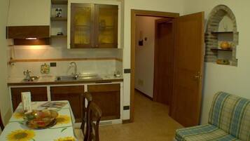 Cocina compacta con lavamanos, armarios y una mesa de comedor con mantel floreado.