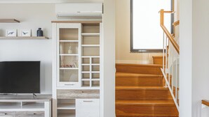 A modern living room with a flat-screen TV, built-in shelving, and a wooden staircase. - New Casa Bondi by Your Madeira Rentals (Ponta do Sol, Madeira Island)