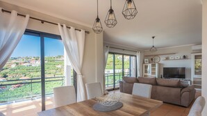 A spacious living area with a wooden dining table, a sofa, and a TV. - New Casa Bondi by Your Madeira Rentals (Ponta do Sol, Madeira Island)