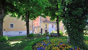 Un jardin avec des fleurs aux couleurs vives, des arbres et un bâtiment doté de balcons en arrière-plan.