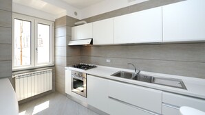 Une cuisine moderne avec des meubles blancs, un four encastré, une cuisinière à gaz et un évier en acier inoxydable.