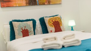 Una cama bien hecha con dos almohadones decorativos, una toalla doblada y una lámpara de noche.