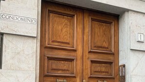 Een houten dubbele deur met een koperen handgreep, een naambordje met daarop 'CONDOMINIO' en een brievenbus aan de rechterkant.