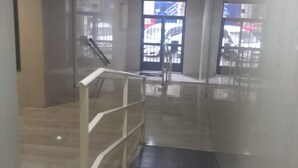 Un intérieur moderne avec un escalier menant à un niveau inférieur, une porte en verre avec un portail en métal, et une vue sur les voitures garées à l’extérieur.