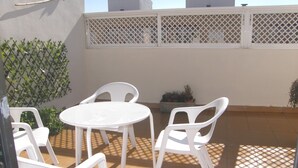 Une terrasse avec des chaises et une table en plastique blanc, entourée d’une clôture blanche et de plantes en pot.