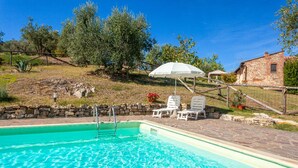 Une piscine bordée d’un mur en pierre, d’une clôture en bois et d’un bâtiment en pierre en arrière-plan.