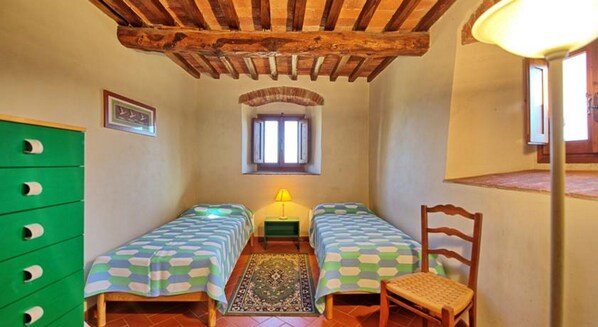 Ein Zimmer mit zwei Einzelbetten, einem grünen Schrank, einem kleinen Fenster und einer Lampe.