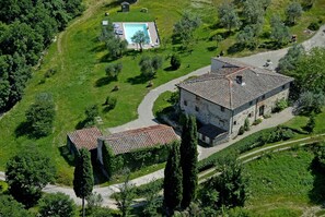 Un bâtiment en pierre avec un toit en tuiles, entouré d’un jardin bien entretenu et d’une piscine.